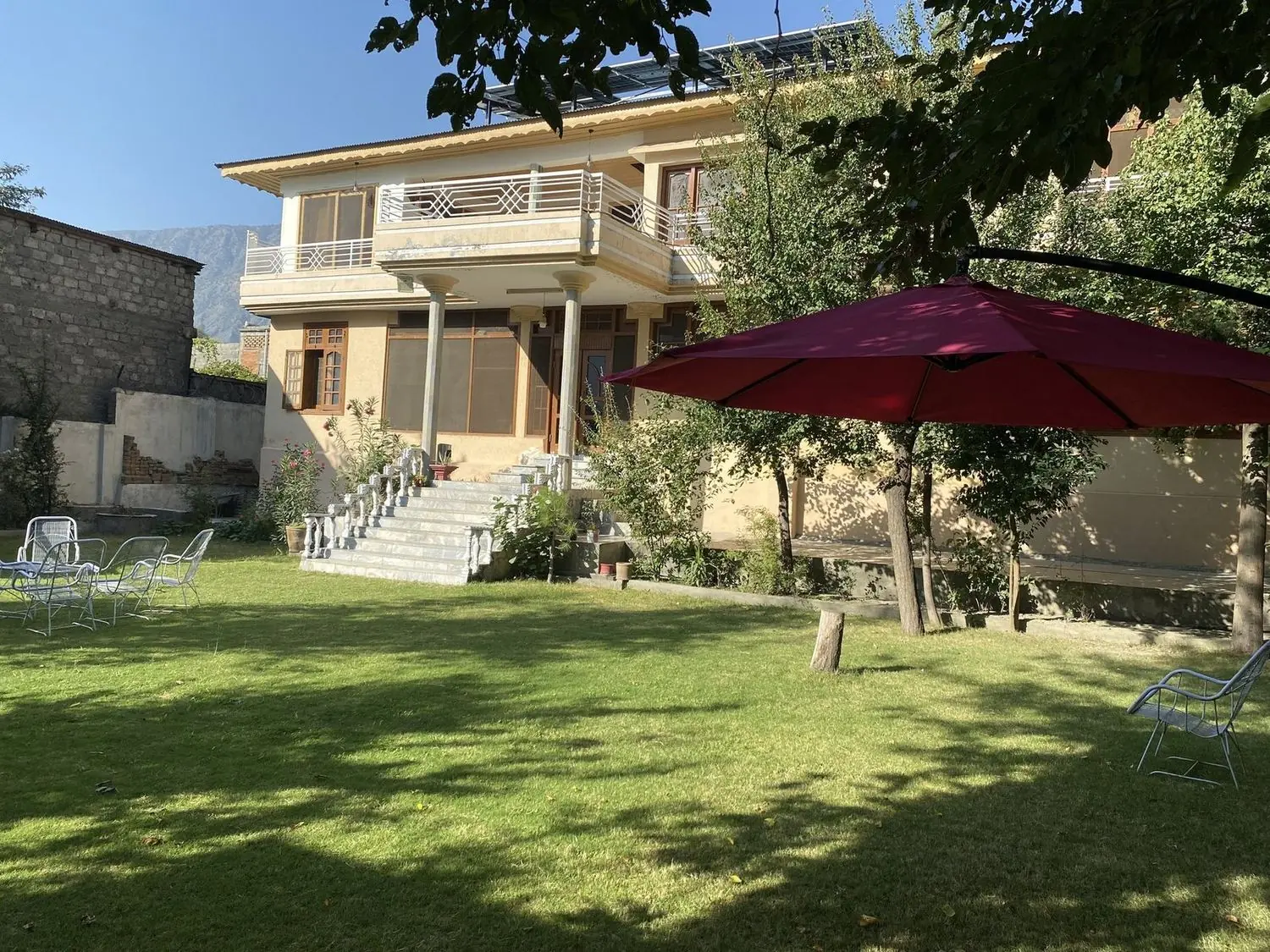 The guesthouse across its lawn, with a red parasol and mountains behind